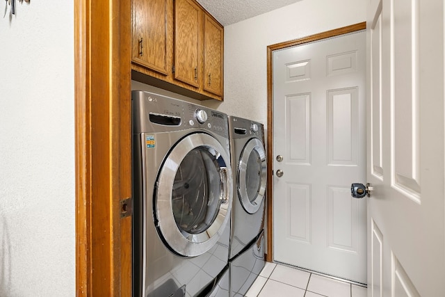 clothes washing area featuring washer and dryer, a textured ceiling, cabinets, and light tile patterned flooring