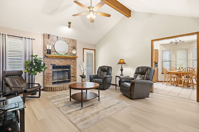 living room featuring beam ceiling, a brick fireplace, high vaulted ceiling, ceiling fan with notable chandelier, and light wood-type flooring