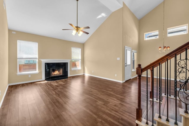 unfurnished living room featuring a wealth of natural light, ceiling fan with notable chandelier, dark wood-type flooring, and a tile fireplace