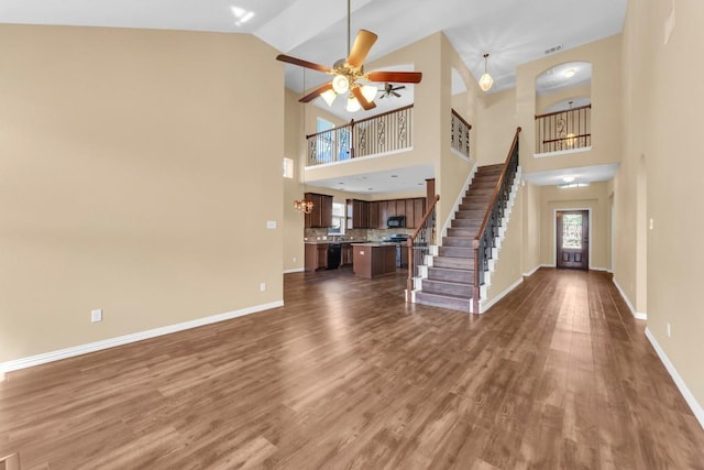 unfurnished living room featuring a wealth of natural light, ceiling fan, dark wood-type flooring, and a high ceiling