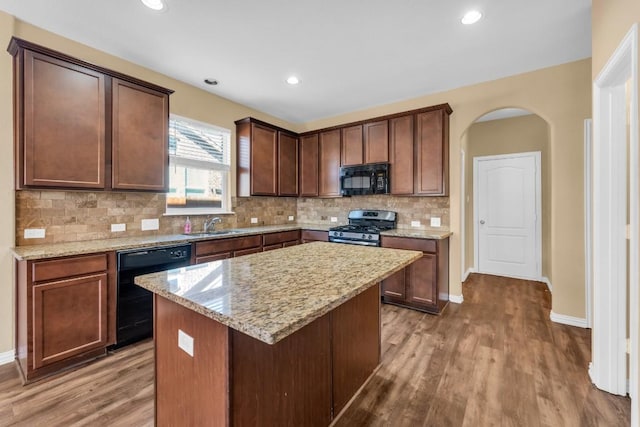 kitchen with dark hardwood / wood-style flooring, tasteful backsplash, light stone counters, black appliances, and a kitchen island