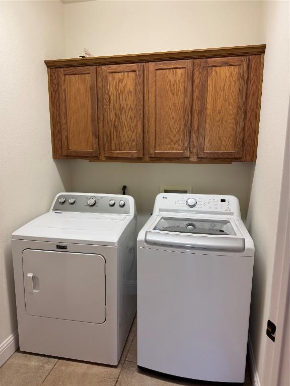 laundry room with washer and dryer, cabinets, and light tile patterned flooring