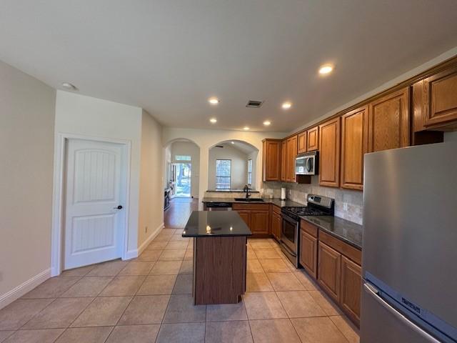 kitchen with decorative backsplash, stainless steel appliances, sink, light tile patterned floors, and a kitchen island