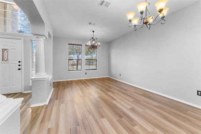 entrance foyer with decorative columns, an inviting chandelier, and light hardwood / wood-style flooring