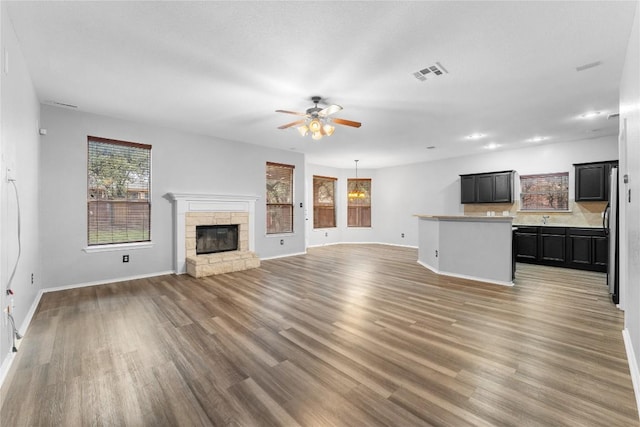 unfurnished living room featuring ceiling fan, dark hardwood / wood-style floors, and a stone fireplace