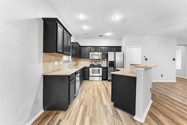 kitchen featuring appliances with stainless steel finishes, light wood-type flooring, backsplash, light stone counters, and sink