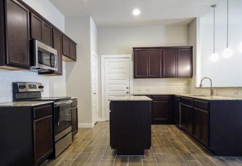 kitchen with sink, decorative backsplash, appliances with stainless steel finishes, decorative light fixtures, and a kitchen island