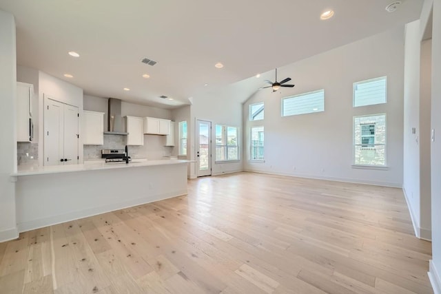 kitchen featuring white cabinetry, ceiling fan, light hardwood / wood-style flooring, wall chimney range hood, and tasteful backsplash