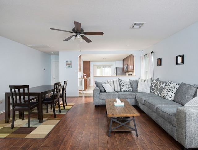 living room with dark wood-style flooring, visible vents, and ceiling fan