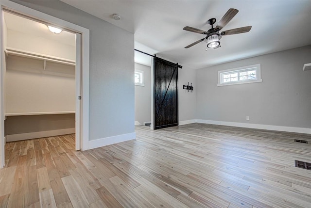 unfurnished bedroom featuring ceiling fan, a barn door, a spacious closet, light hardwood / wood-style floors, and a closet