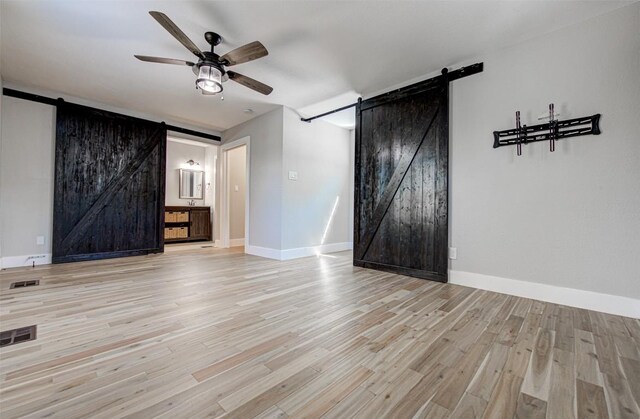 unfurnished living room with a barn door, light hardwood / wood-style flooring, and ceiling fan