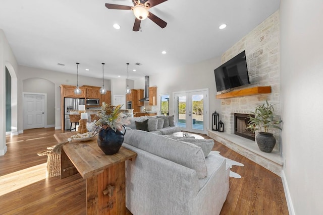 living room with a stone fireplace, ceiling fan, french doors, and hardwood / wood-style flooring