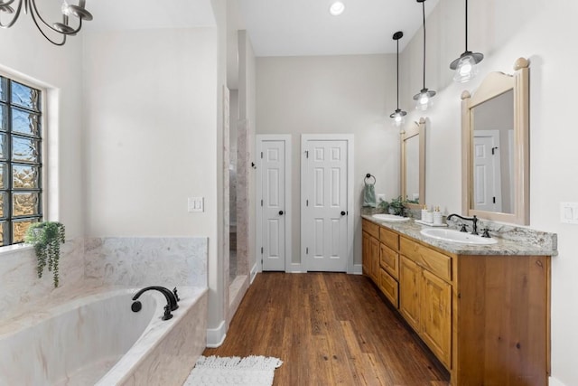 bathroom with hardwood / wood-style flooring, vanity, tiled bath, and an inviting chandelier