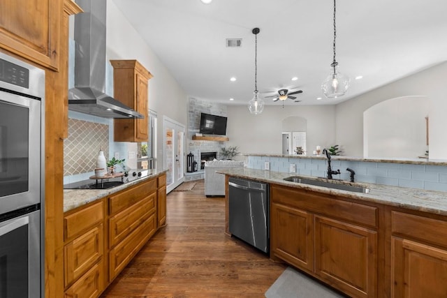 kitchen featuring stainless steel appliances, ceiling fan, wall chimney range hood, pendant lighting, and a fireplace