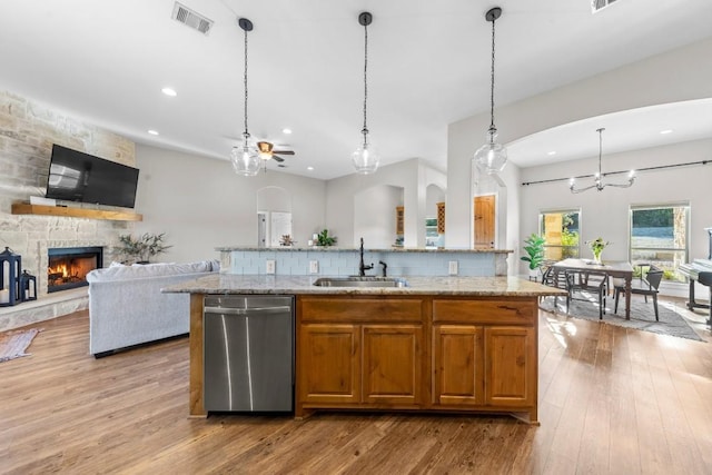 kitchen with pendant lighting, a kitchen island with sink, sink, stainless steel dishwasher, and a fireplace