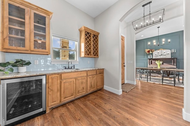 bar with backsplash, sink, decorative light fixtures, light stone counters, and beverage cooler