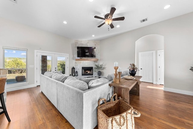 living room with ceiling fan, dark hardwood / wood-style floors, a stone fireplace, and french doors