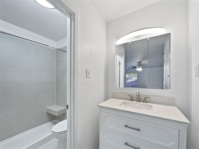 bathroom with tiled shower, vanity, toilet, and ceiling fan