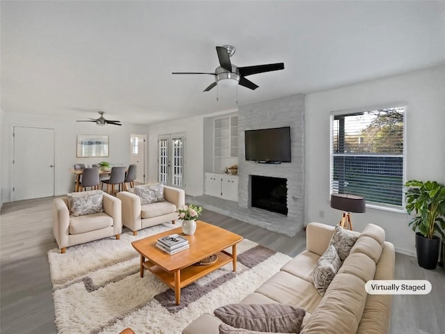 living room with a stone fireplace, ceiling fan, built in features, and hardwood / wood-style floors