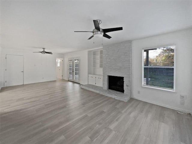 unfurnished living room featuring ceiling fan, built in features, a fireplace, and light hardwood / wood-style flooring