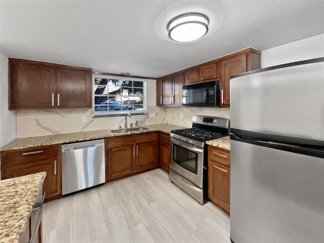 kitchen featuring backsplash, light stone counters, stainless steel appliances, sink, and light hardwood / wood-style floors