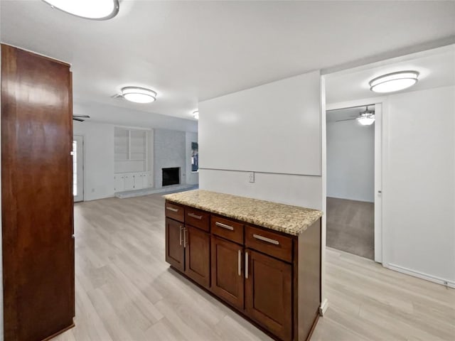 kitchen featuring a large fireplace, light hardwood / wood-style floors, light stone counters, and ceiling fan