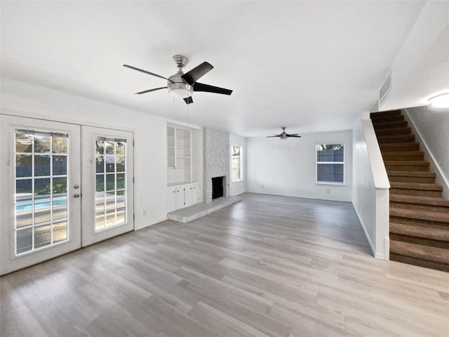 unfurnished living room with built in shelves, ceiling fan, french doors, light hardwood / wood-style floors, and a fireplace