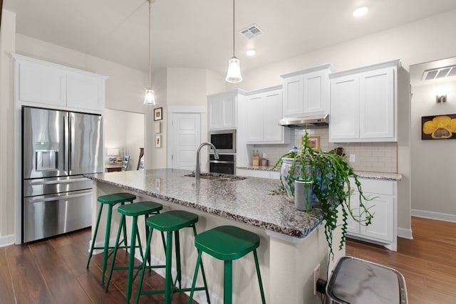 kitchen with tasteful backsplash, stainless steel appliances, decorative light fixtures, white cabinets, and an island with sink