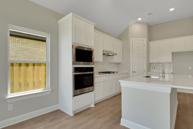 kitchen featuring tasteful backsplash, under cabinet range hood, visible vents, gas stovetop, and a sink