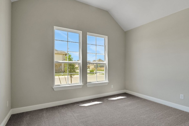 carpeted spare room with a wealth of natural light, vaulted ceiling, and baseboards