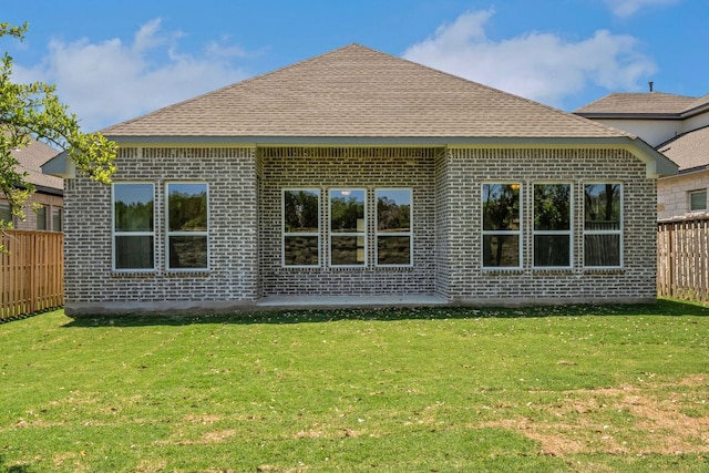 rear view of property featuring brick siding, fence, a shingled roof, and a lawn