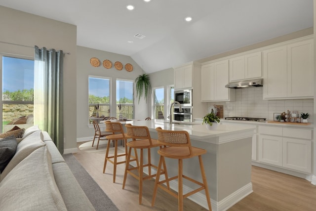 212 Millbend Rd, Georgetown, TX 78633 - kitchen with vaulted ceiling, a kitchen island with sink, tasteful backsplash, stainless steel appliances, and under cabinet range hood