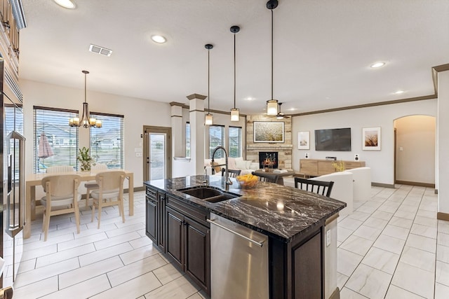 kitchen featuring stainless steel appliances, sink, a center island with sink, dark stone countertops, and a fireplace