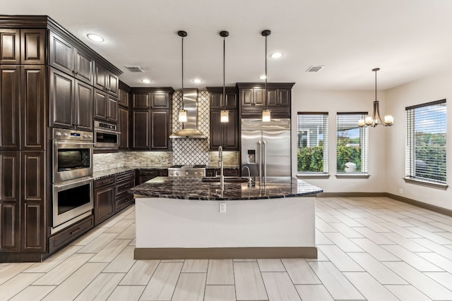 kitchen with sink, wall chimney range hood, decorative light fixtures, dark brown cabinets, and appliances with stainless steel finishes