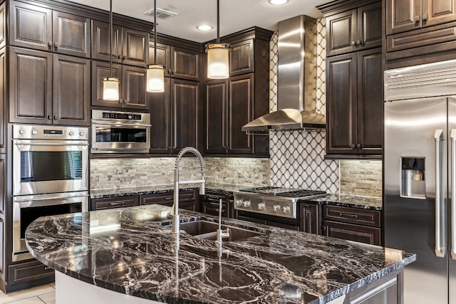 kitchen with sink, wall chimney exhaust hood, hanging light fixtures, stainless steel appliances, and dark stone counters