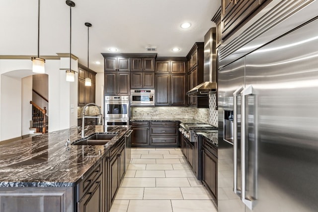 kitchen with sink, decorative light fixtures, wall chimney exhaust hood, appliances with stainless steel finishes, and dark brown cabinets