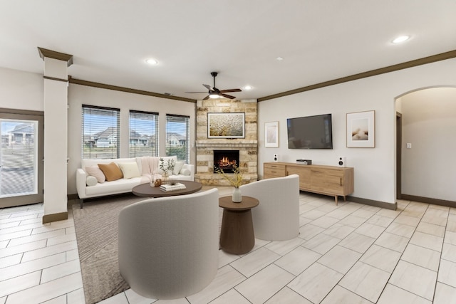 living room featuring a stone fireplace, ceiling fan, and ornamental molding