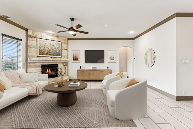 living room featuring a stone fireplace, ceiling fan, and ornamental molding