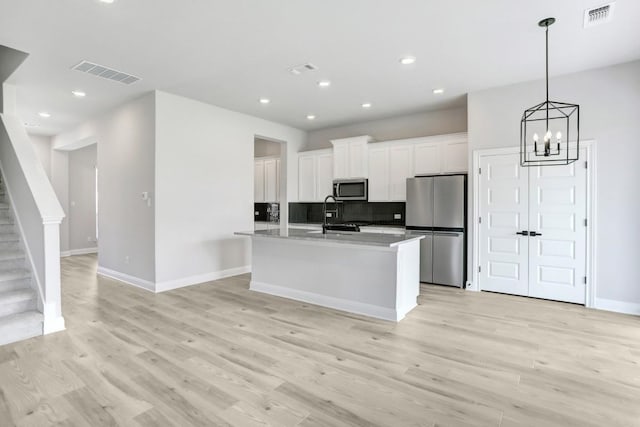 kitchen featuring backsplash, a kitchen island with sink, light hardwood / wood-style flooring, white cabinetry, and stainless steel appliances