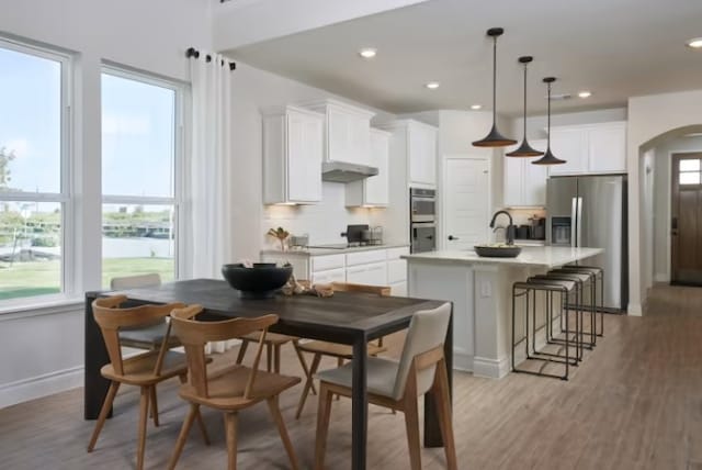 kitchen featuring a center island with sink, white cabinets, hanging light fixtures, appliances with stainless steel finishes, and light hardwood / wood-style floors