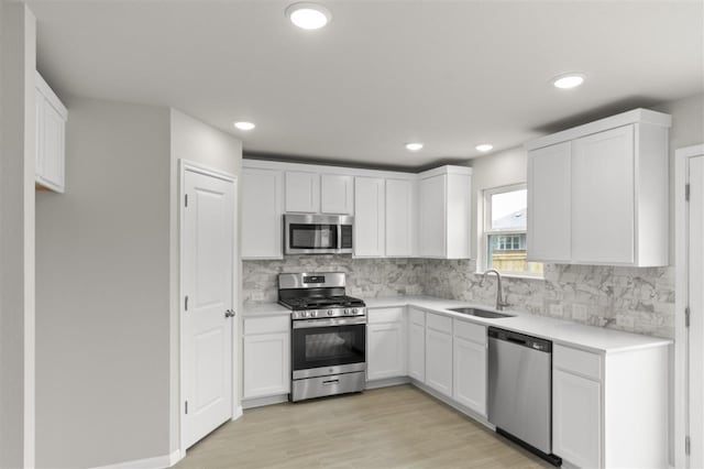 kitchen with white cabinetry, stainless steel appliances, light hardwood / wood-style floors, sink, and backsplash