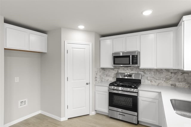 kitchen featuring white cabinetry, appliances with stainless steel finishes, backsplash, light hardwood / wood-style flooring, and sink