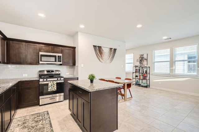 kitchen with dark brown cabinetry, stainless steel appliances, a kitchen island, light stone counters, and light tile patterned flooring