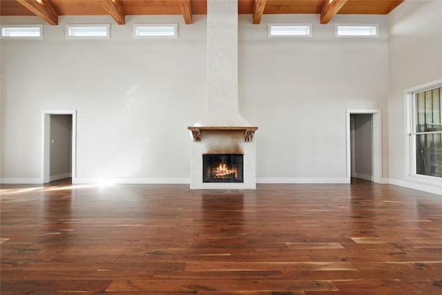 unfurnished living room featuring dark hardwood / wood-style floors, wooden ceiling, a fireplace, and a high ceiling