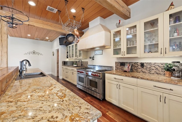 kitchen with light stone countertops, sink, beamed ceiling, range with two ovens, and custom exhaust hood