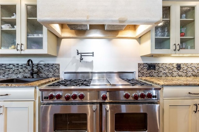 kitchen featuring sink, range hood, range with two ovens, decorative backsplash, and white cabinets