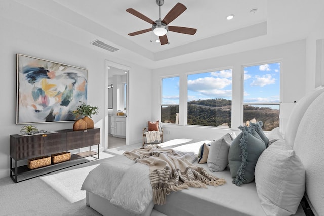 bedroom with a raised ceiling, ensuite bathroom, ceiling fan, and multiple windows