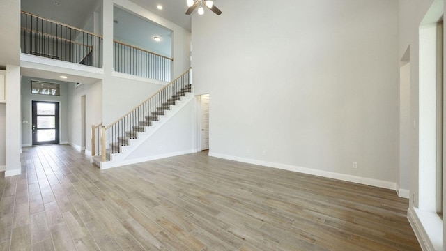 1024 Lariat Loop, Liberty Hill, TX 78642 - unfurnished living room with stairway, a ceiling fan, a towering ceiling, wood finished floors, and baseboards