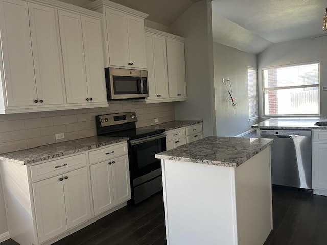 kitchen with appliances with stainless steel finishes, backsplash, white cabinets, a center island, and lofted ceiling