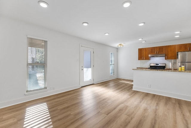 kitchen featuring decorative backsplash, light stone counters, light hardwood / wood-style flooring, and appliances with stainless steel finishes